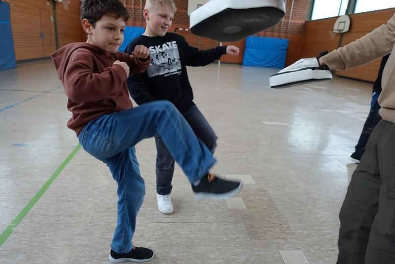 Kindergruppe übt in der Turnhalle eine Abwehrbewegung mit ausgestrecktem Arm