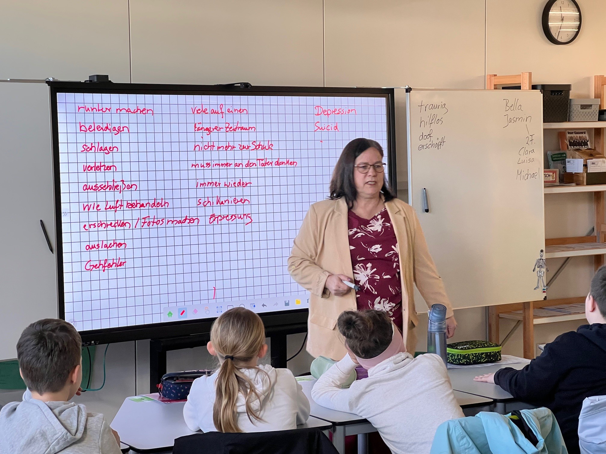 Lehrkraft bespricht mit Schülerinnen und Schülern Begriffe rund um Mobbing am Whiteboard